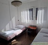 A simple room with two beds, a table, windows, and commercial spaces next door.