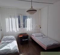 The room contains two beds, a table, a chair, and curtains.