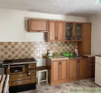 A kitchen with wooden cabinets, an old stove, dishes, and a sink in a family house.