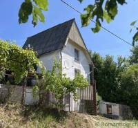 A cottage in Rožňava surrounded by greenery and vineyards, with a blue sky in the background.