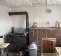 A simple kitchen in a cottage with a stove, sink, and chair in a rustic style.
