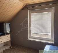 A television and a dresser in the attic room of a cottage with a window and a wooden ceiling.