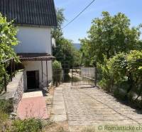 Cottage near Rožňava with an access road, green surroundings, and a gate.