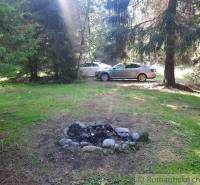 In the picture, there is a campfire, forests, and cars, an ideal location for a cabin in nature.