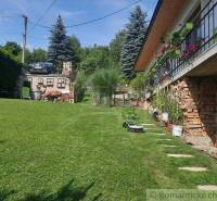 In front of the house, there is a green lawn, flowers on the balcony, and a car by the tree.