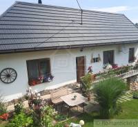 The garden is equipped with a table, windows, and trimmed flowers on the facade of the family house.