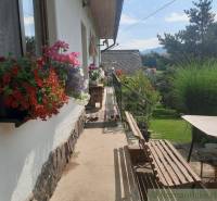 Flower arrangement and a bench on the porch of a family house surrounded by a garden and mountains.