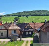 The image shows a row of family houses in the countryside with a green meadow and a hill.