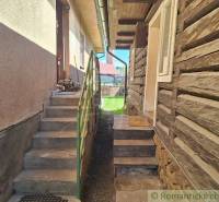 Entrance next to a wooden cottage and family house, stairs, flowers, yard.