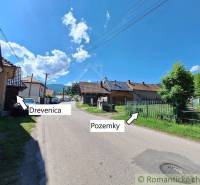 A view of a village street, adorned with wooden houses, surrounded by plots of land and family homes.