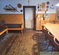 The interior of a traditional cottage with wooden furniture, a bed, chairs, and walls with decorations.
