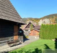A wooden cottage in nature, a garden, coniferous trees, a family house, mountains, and a sunny day.