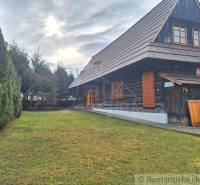 In the picture, there is a wooden cottage next to a mowed lawn and a trimmed hedge.