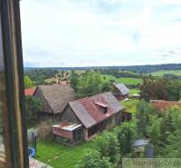 The image shows a view of a rural family house and green countryside.