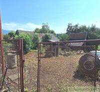 A view through the gate to a yard with vines, a house, and nature in the countryside.
