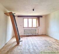 An empty room in a family house with a slanted radiator, wooden floor, and a window.