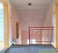 Hallway of a family house with a wallpapered wall, wooden floor, and red staircase railing.