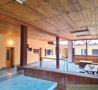 Wooden terrace ceiling with a ping pong table, benches, and a family house in the yard.