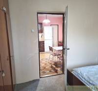 A room with a bed leads to a kitchen with a refrigerator in a family house.
