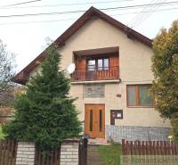 A family house with a wooden balcony, a satellite dish, and a garden behind a wooden fence.