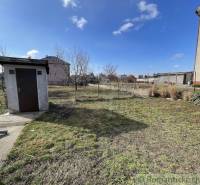 A garden with a family house, a shed and a fence, lawn under the blue sky, houses in the background.