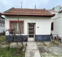 A small family house, a garden with vines, next to the house are plastic chairs and a satellite.