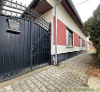 A family house with an iron gate and a small gate stands out with an entrance to a paved walkway.