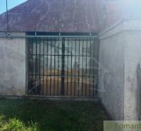 An old building with a neglected roof, metal grille, and fence surrounding a family house.
