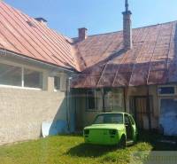 A yard with part of a family house, an old car, and a mowed lawn in the surroundings.