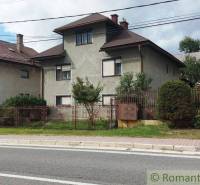 A family house with a garden in a quiet village area, surrounded by a road and a fence.