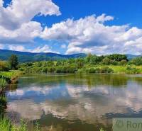 In the picture, there is a tranquil river with a bridge, surrounded by green hills and a blue sky. The area is suitable for plots and living.