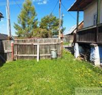 An old yard with grass, a wooden fence, and peculiar properties in the background.
