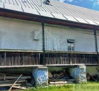 An older cottage with a wooden porch, a metal roof, and a settled white facade.