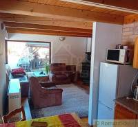 The interior of a cabin with a wooden ceiling, a comfortable sofa, and a kitchenette.