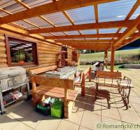 A wooden terrace of the cottage with a grill, seating area, and a view of nature, ideal for relaxation.