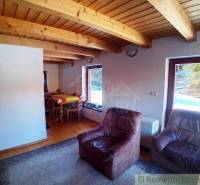 Living room in a cottage with leather armchairs, wooden ceiling, and dining table.