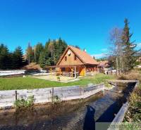 A cottage surrounded by nature with a stream in the foreground, rich forests provide a peaceful retreat.