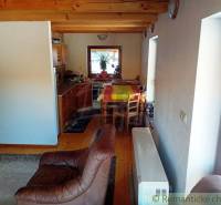 We see the interior of a cabin with a wooden ceiling, a kitchen, and comfortable furniture.