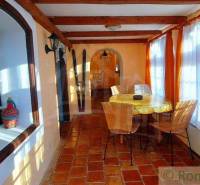The interior of a cottage with a dining table, brick floors, large windows, curtains, interesting properties.