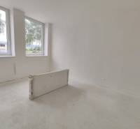 An empty room with two windows in a three-room apartment, white walls, tiles waiting for installation.