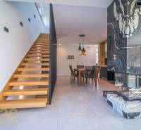 Interior of a family house with wooden stairs, a dining table, and a tiled stove.