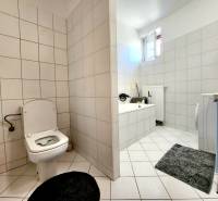 A bathroom in a studio apartment with a bathtub, washing machine, and toilet, tiled with light-colored tiles.
