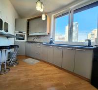 A one-bedroom apartment kitchen with a bar, view of large windows and city skyline.