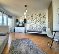 Living room with a bed, floral wallpaper, table, armchair, window with a view.