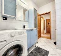 A bathroom in a studio apartment with appliances, cabinets, and ceramic tiles.
