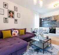 Living room with a purple couch, kitchen, table, and decorations in a 3-room apartment.