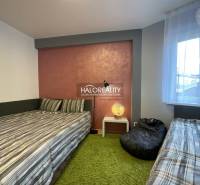A bedroom in a 3-room apartment with two beds, a lamp, and a green carpet.