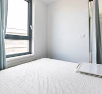 Bright bedroom in a 2-room apartment with curtains and a bed with a white bedspread.