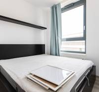 Bedroom with a bed and a shelf in a 2-room apartment, light curtains and a large window.