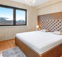 A bedroom with a large bed, a lamp, and a view of the city, in a three-room apartment.